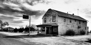 Black and white photo of an abandoned wooden house in a barren rural landscape.